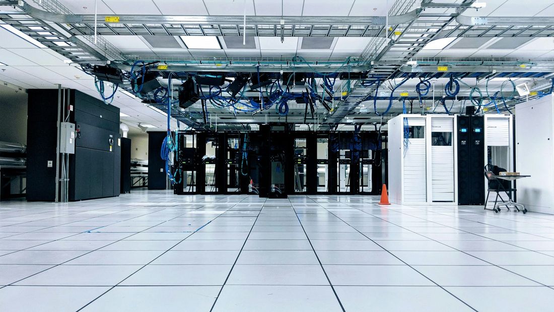 Clean data centre hall with server cabinets under overhead cable trays and a white raised floor