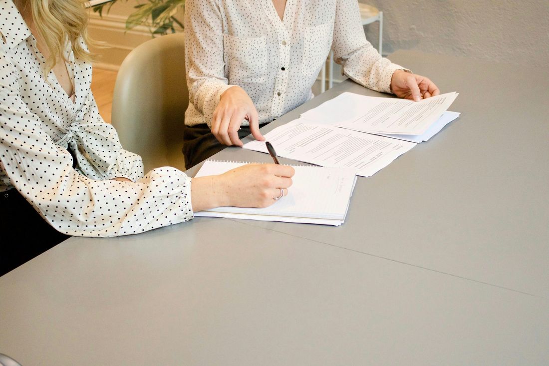 Two people reviewing and annotating printed documents at a desk, shown as an audit or documentation review