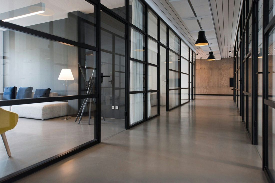 Long corridor of a modern office with black-framed glass partitions, meeting rooms and a lounge area