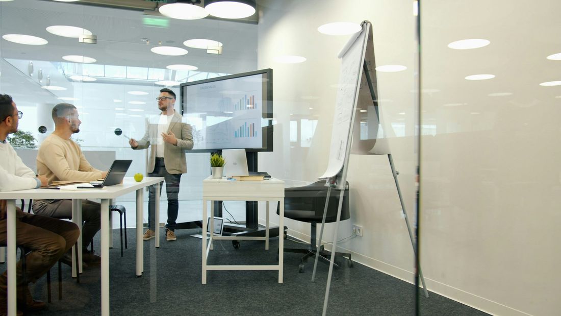 Presenter at a screen and flipchart in a bright modern office while colleagues listen, representing a strategy workshop